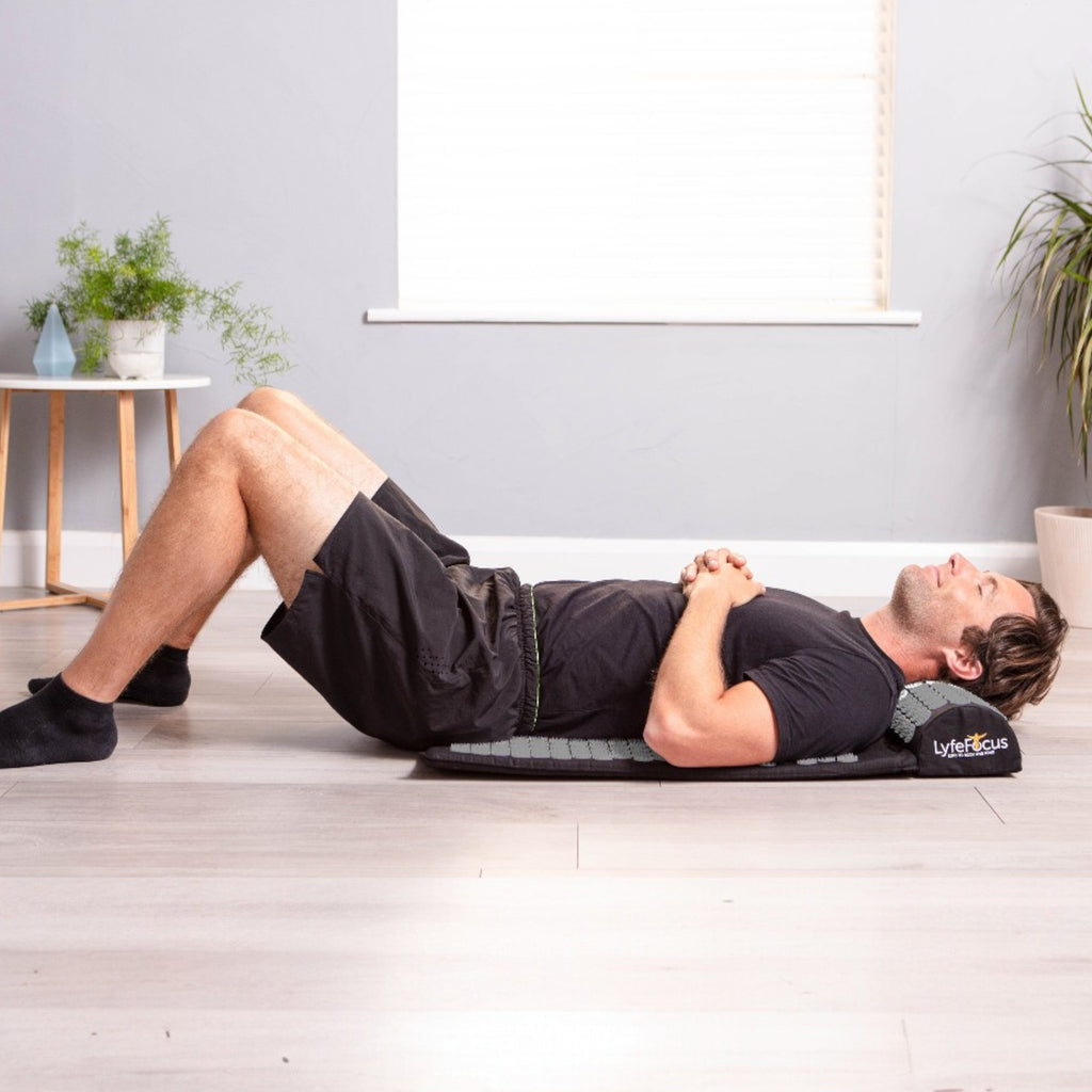 Man exercising on a mat with a pillow under his head in a room with plants and a window.