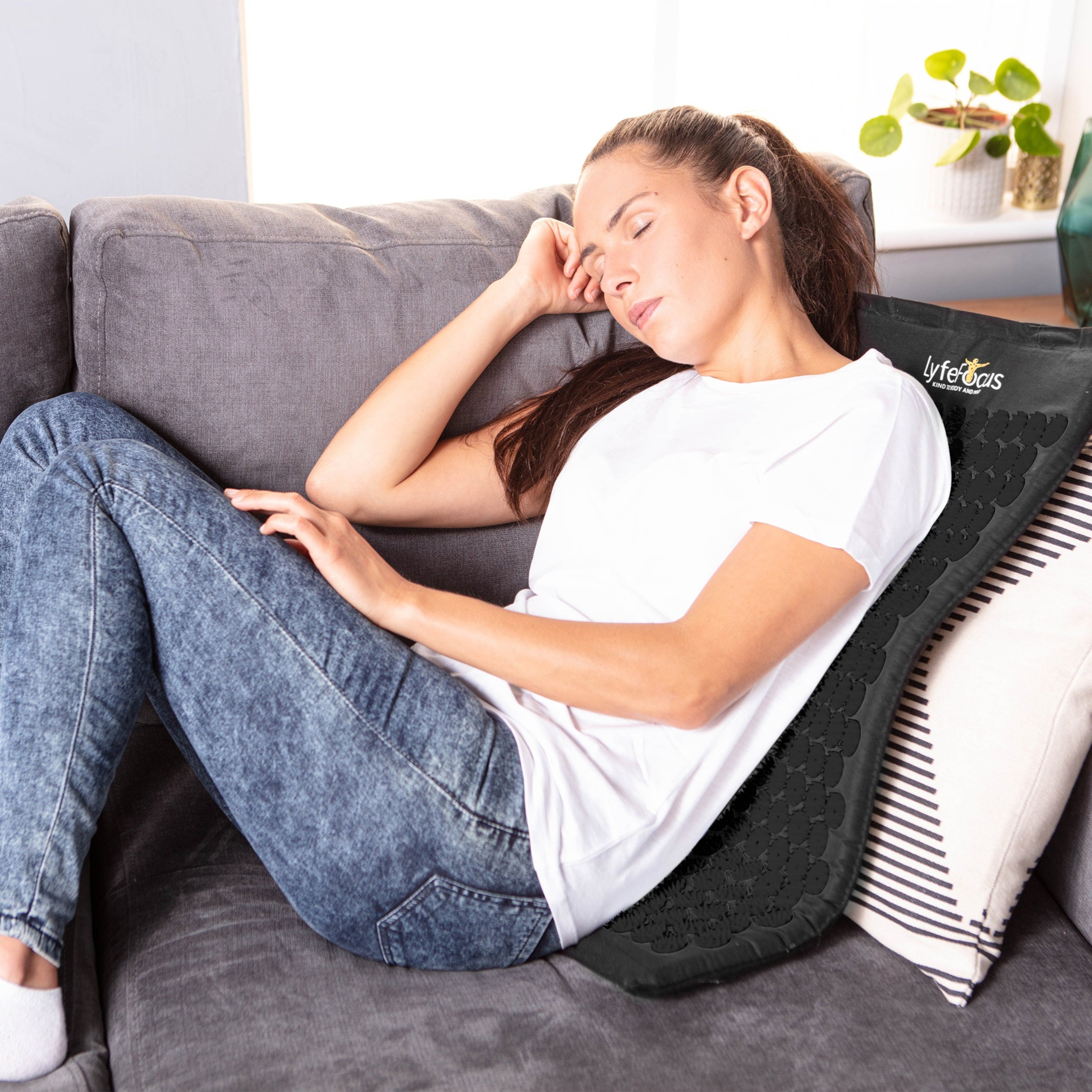 Woman using a back massager on a couch in a home setting