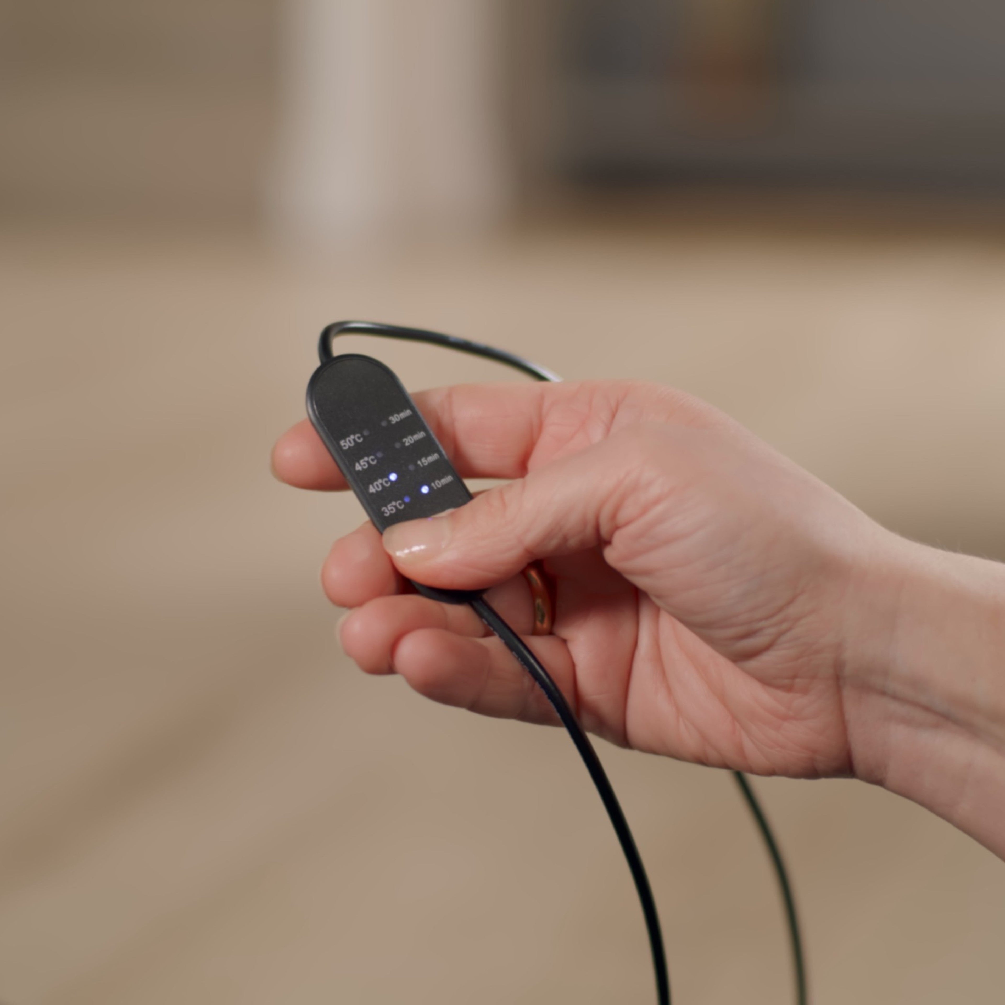 Hand holding a black electronic device with buttons on a blurred background