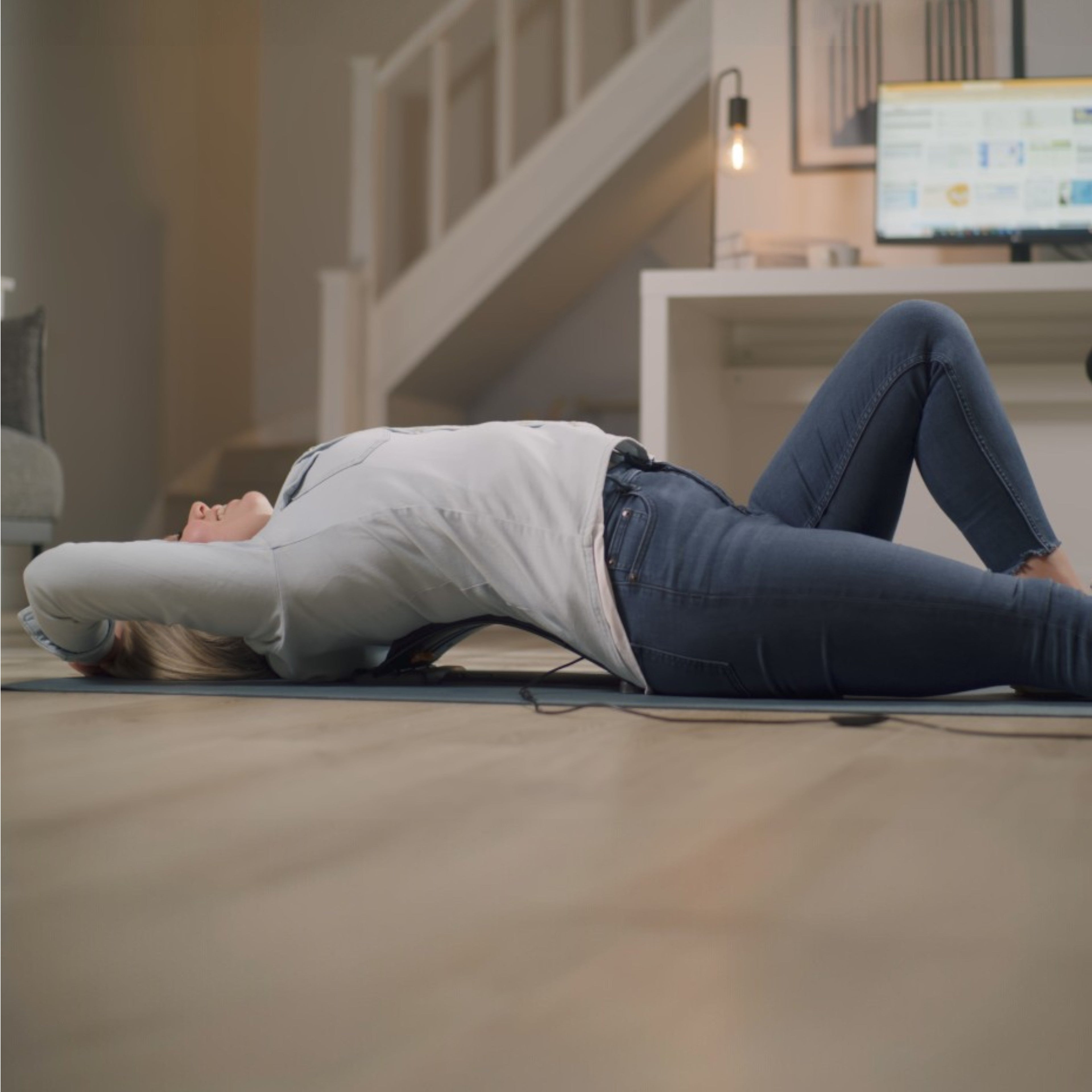 Person lying on a mat in a home setting with a computer monitor in the background