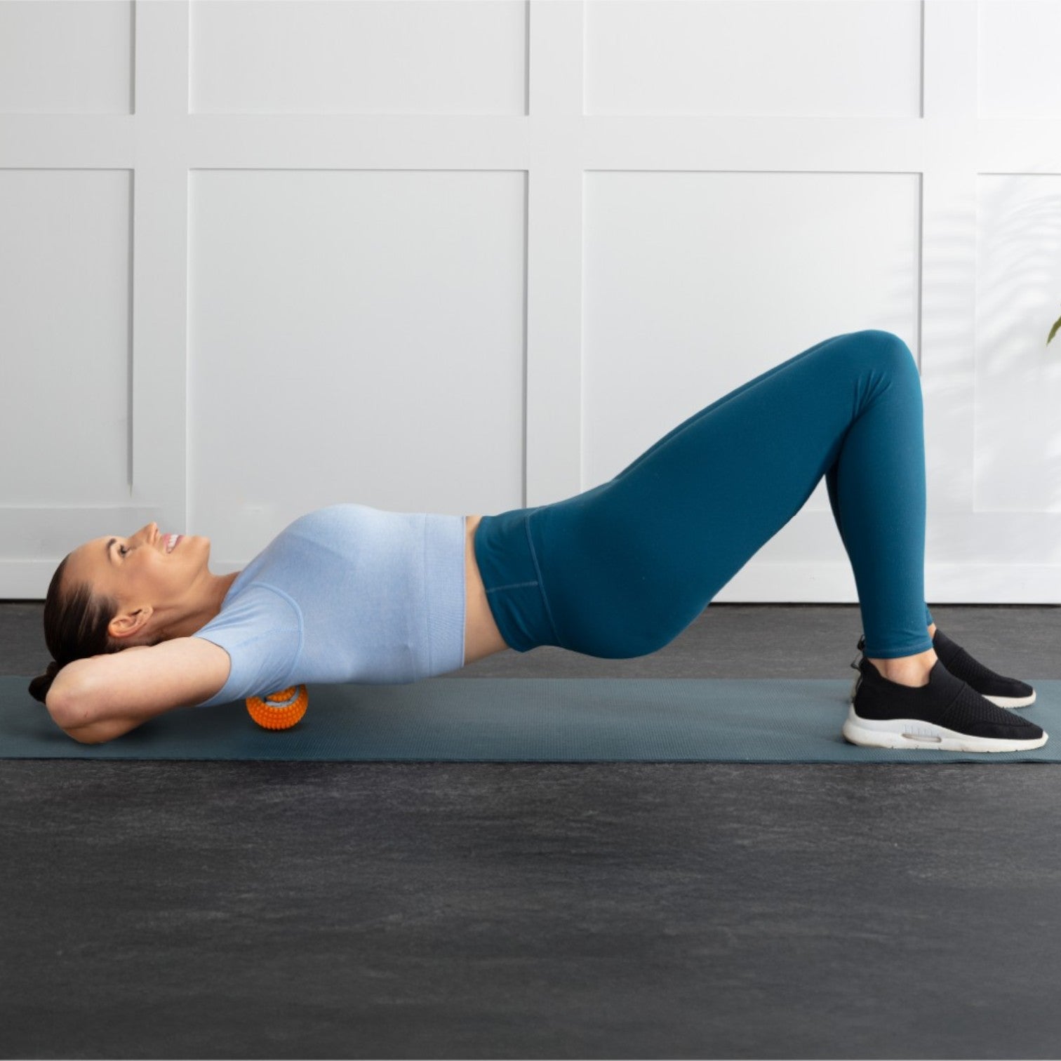 Woman performing an exercise with a weight on a mat against a white paneled wall.